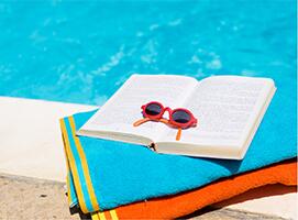 A book, towels and sunglasses by the pool